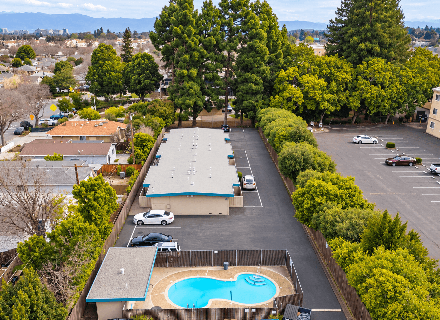 Aerial view over the swimming pool and single-story homes toward surrounding trees