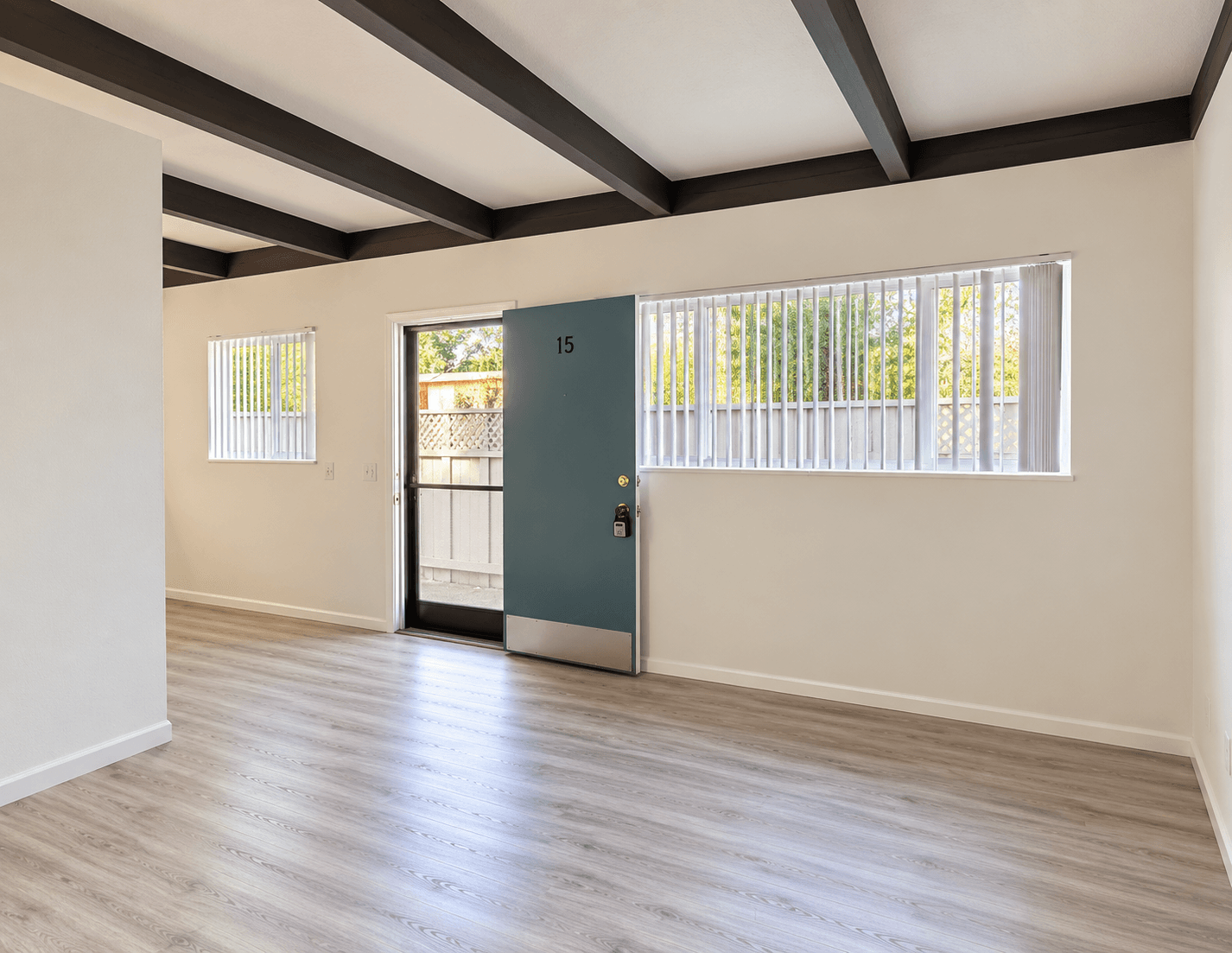 Light-filled studio with exposed ceiling beams and a door opening to a private patio
